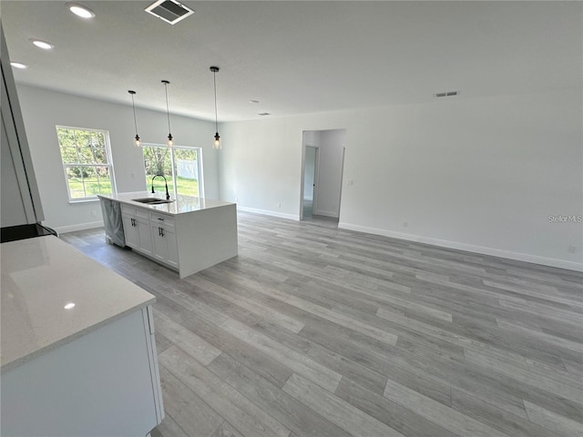 kitchen with sink, decorative light fixtures, light hardwood / wood-style floors, white cabinetry, and an island with sink