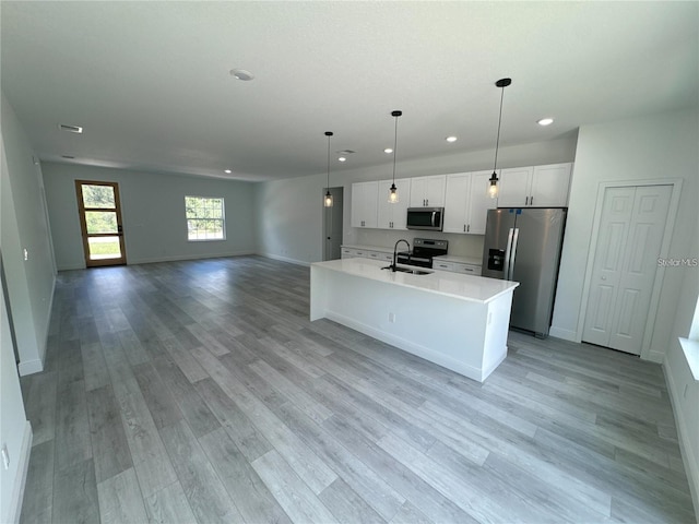 kitchen featuring appliances with stainless steel finishes, sink, pendant lighting, white cabinets, and light hardwood / wood-style floors