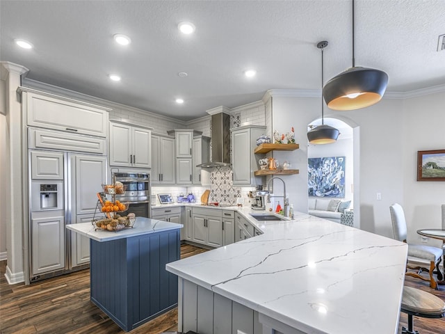 kitchen featuring sink, gray cabinetry, hanging light fixtures, kitchen peninsula, and wall chimney exhaust hood