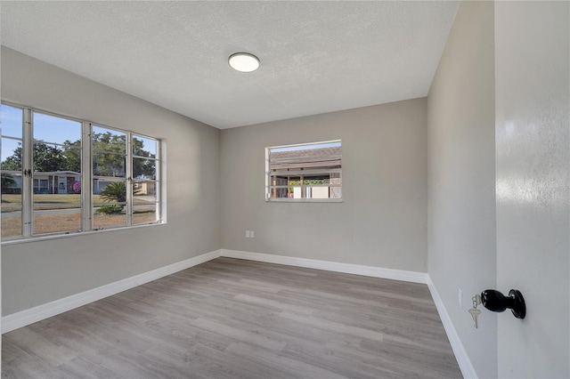 empty room with a textured ceiling and light hardwood / wood-style flooring