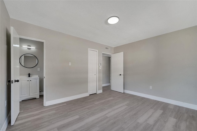 unfurnished bedroom with a closet, sink, a textured ceiling, and light wood-type flooring