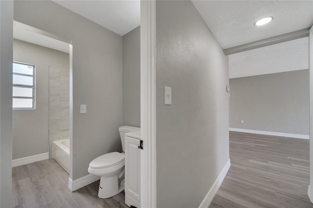 bathroom with hardwood / wood-style flooring, washtub / shower combination, toilet, and a textured ceiling