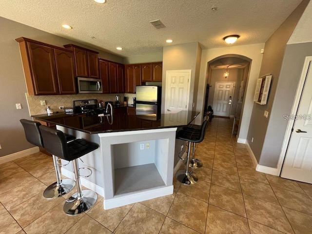 kitchen featuring a kitchen bar, a textured ceiling, stainless steel appliances, and light tile patterned flooring