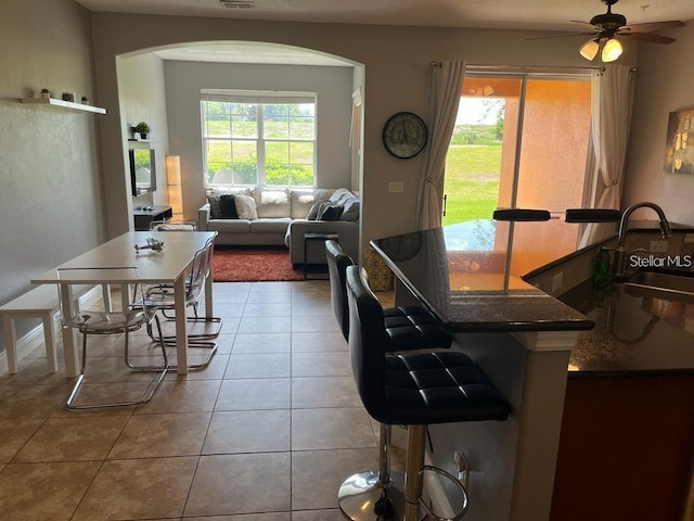 kitchen featuring a breakfast bar, ceiling fan, a healthy amount of sunlight, sink, and tile patterned flooring