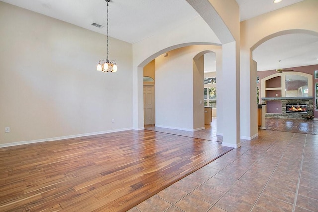 spare room with built in shelves, a fireplace, hardwood / wood-style floors, and an inviting chandelier