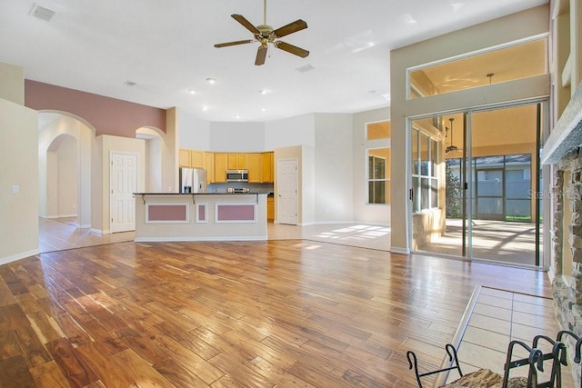 unfurnished living room with a high ceiling, light wood-type flooring, and ceiling fan