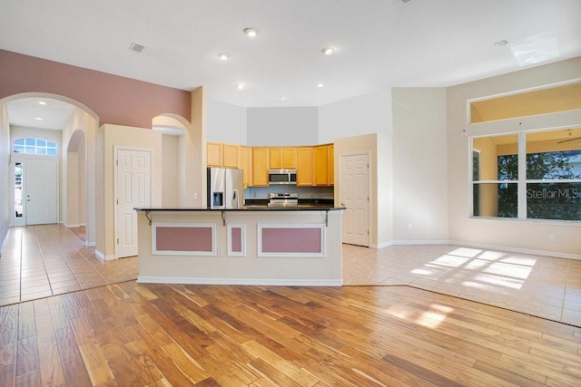 kitchen featuring a kitchen island with sink, light brown cabinets, stainless steel appliances, and light wood-type flooring