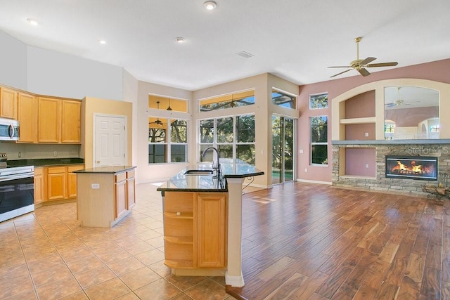 kitchen featuring electric range, sink, a stone fireplace, built in features, and a kitchen island with sink