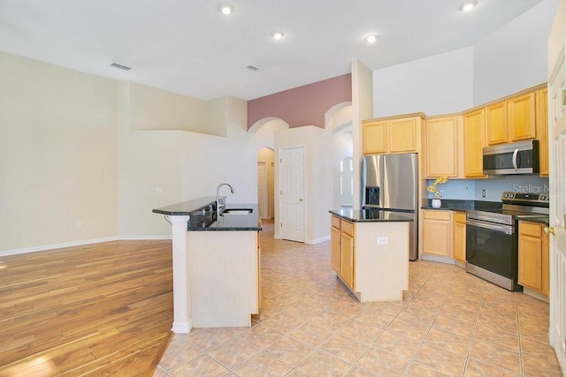 kitchen with appliances with stainless steel finishes, a towering ceiling, a kitchen island with sink, and sink