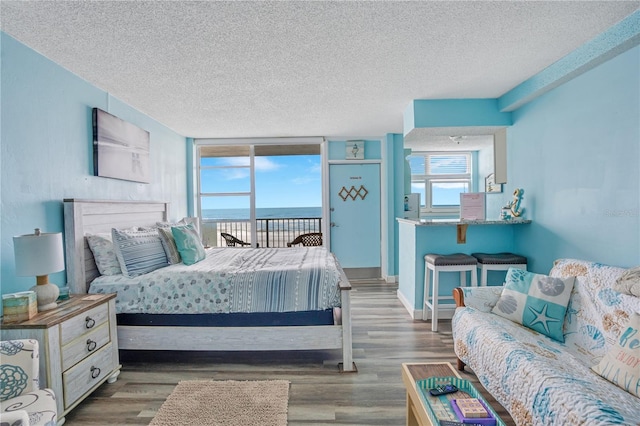 bedroom featuring access to exterior, dark hardwood / wood-style flooring, a water view, and a textured ceiling