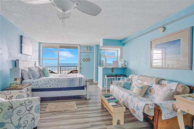 bedroom with access to outside, a water view, ceiling fan, light wood-type flooring, and a textured ceiling