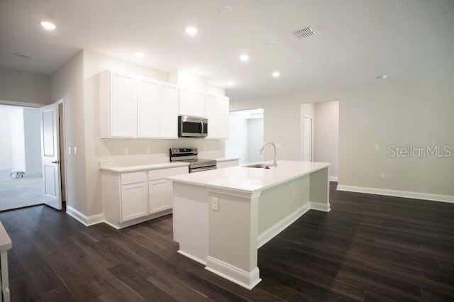 kitchen with white cabinets, dark hardwood / wood-style floors, stainless steel appliances, and a kitchen island with sink