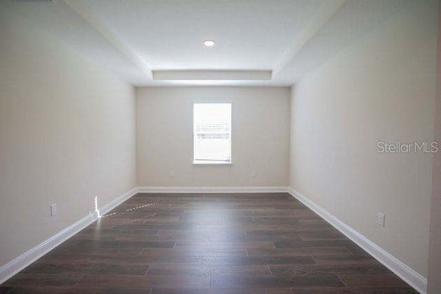 empty room featuring a raised ceiling and dark hardwood / wood-style flooring