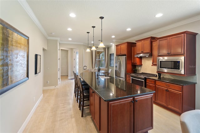 kitchen with a kitchen island with sink, under cabinet range hood, a sink, hanging light fixtures, and appliances with stainless steel finishes