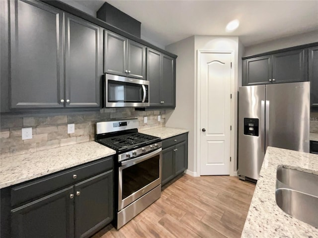 kitchen featuring sink, tasteful backsplash, light stone counters, appliances with stainless steel finishes, and light wood-type flooring