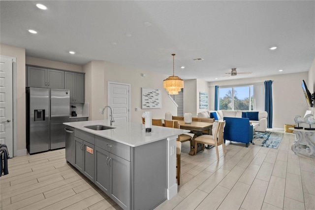 kitchen with stainless steel appliances, gray cabinets, a center island with sink, and sink