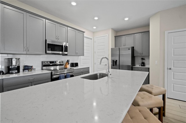 kitchen with light stone countertops, sink, a kitchen breakfast bar, light hardwood / wood-style flooring, and appliances with stainless steel finishes