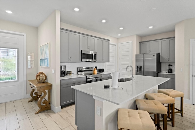 kitchen featuring a kitchen island with sink, sink, gray cabinets, appliances with stainless steel finishes, and a kitchen bar