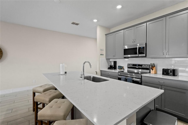 kitchen featuring a breakfast bar, sink, an island with sink, and appliances with stainless steel finishes