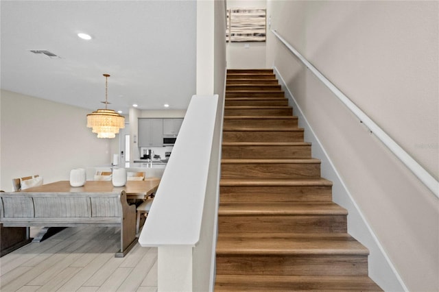 stairs featuring hardwood / wood-style floors and a chandelier