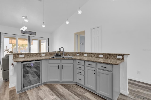 kitchen with light wood-type flooring, beverage cooler, sink, decorative light fixtures, and high vaulted ceiling