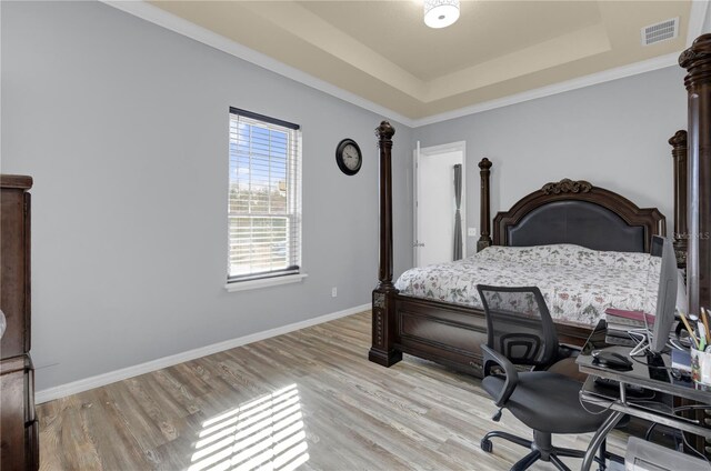 bedroom with a raised ceiling, crown molding, and light wood-type flooring