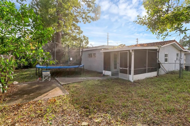 back of house with a sunroom, a trampoline, a patio area, and a lawn