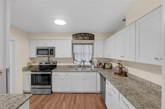 kitchen with sink, light stone countertops, light wood-type flooring, appliances with stainless steel finishes, and white cabinetry