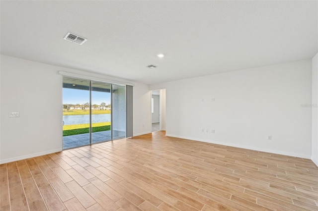 empty room with a wall of windows, light hardwood / wood-style flooring, and a water view