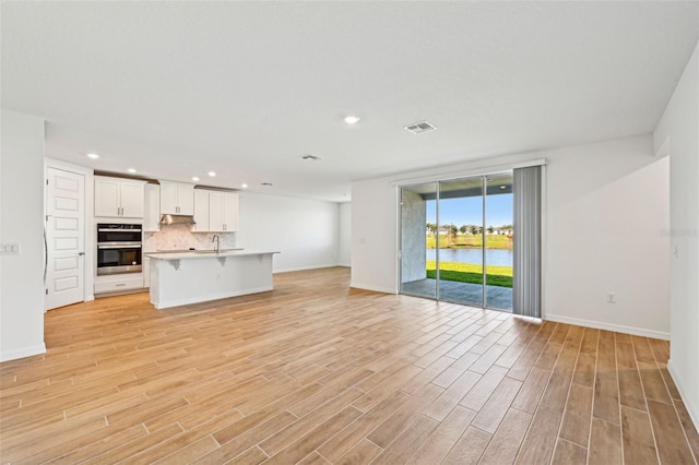 unfurnished living room with sink, light wood-type flooring, and a water view