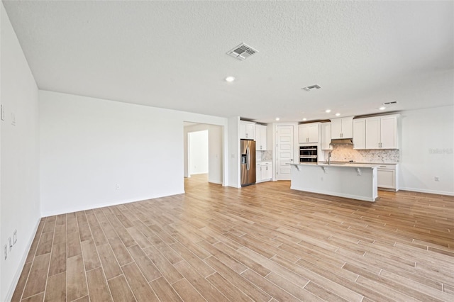 unfurnished living room with sink, a textured ceiling, and light hardwood / wood-style floors