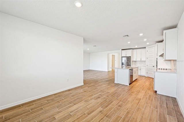 kitchen with appliances with stainless steel finishes, an island with sink, white cabinetry, and decorative backsplash