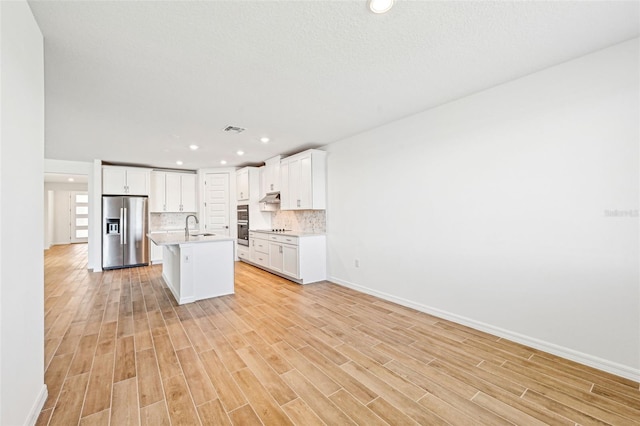 kitchen featuring an island with sink, stainless steel fridge, tasteful backsplash, white cabinetry, and sink