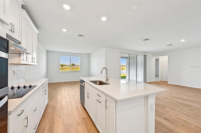 kitchen with stainless steel dishwasher, a center island with sink, black electric cooktop, white cabinetry, and sink