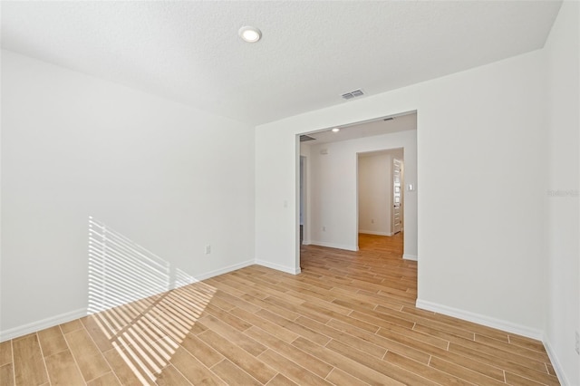 spare room featuring a textured ceiling and light hardwood / wood-style floors