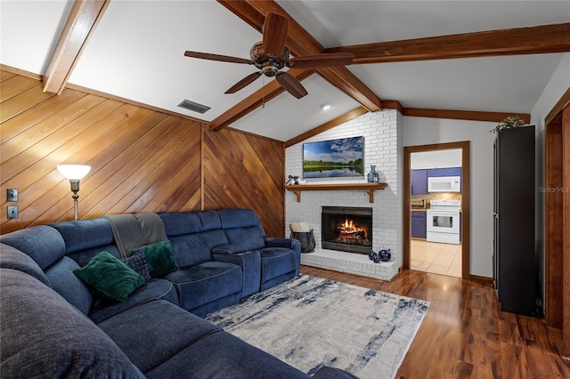 living room featuring hardwood / wood-style floors, vaulted ceiling with beams, ceiling fan, and a brick fireplace