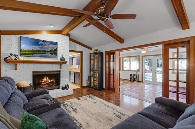 living room featuring a brick fireplace, lofted ceiling with beams, ceiling fan, and french doors