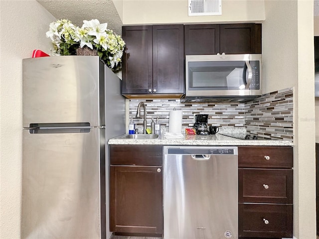 kitchen featuring appliances with stainless steel finishes, dark brown cabinetry, tasteful backsplash, and sink