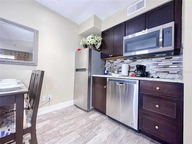 kitchen with dark brown cabinetry, stainless steel appliances, backsplash, a textured ceiling, and light wood-type flooring