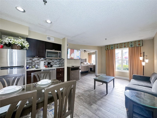 kitchen with backsplash, light hardwood / wood-style floors, a textured ceiling, and appliances with stainless steel finishes