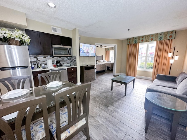 kitchen with backsplash, ceiling fan, light wood-type flooring, a textured ceiling, and stainless steel appliances