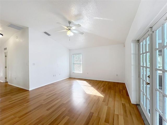 spare room with ceiling fan, light hardwood / wood-style floors, vaulted ceiling, and a textured ceiling