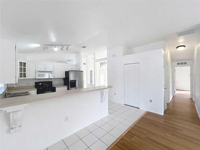 kitchen with sink, white cabinets, black range oven, stainless steel fridge with ice dispenser, and kitchen peninsula