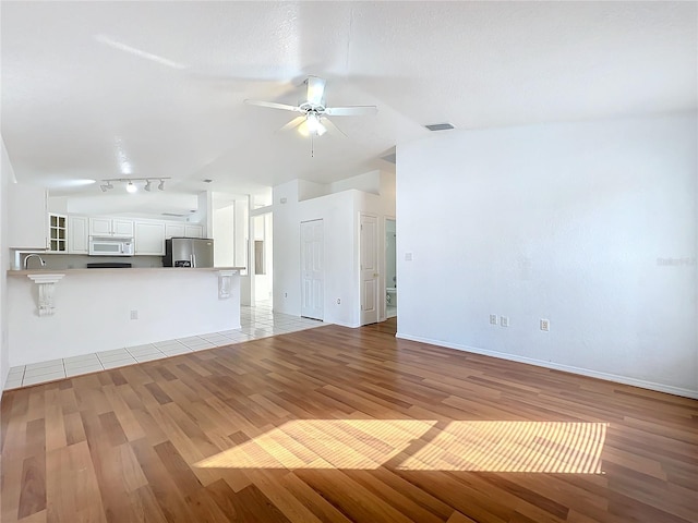 unfurnished living room featuring lofted ceiling, light hardwood / wood-style floors, rail lighting, and ceiling fan