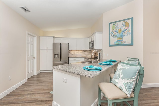 kitchen with a breakfast bar, sink, appliances with stainless steel finishes, light stone counters, and white cabinetry