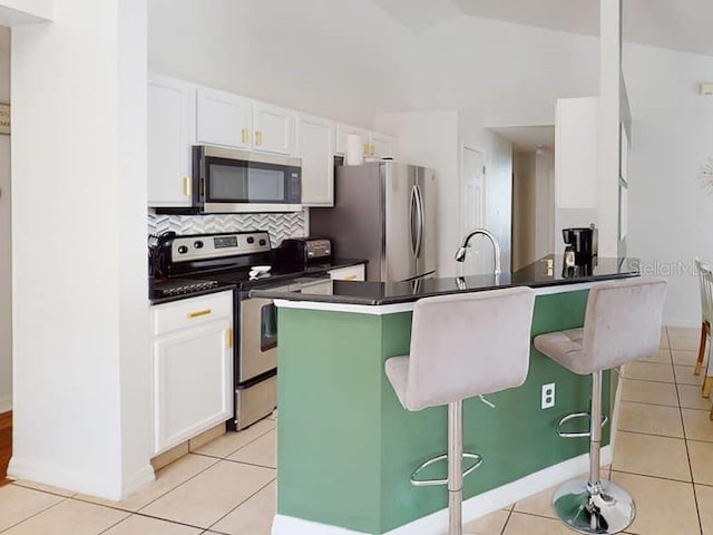 kitchen with white cabinets, a kitchen bar, light tile patterned floors, and stainless steel appliances