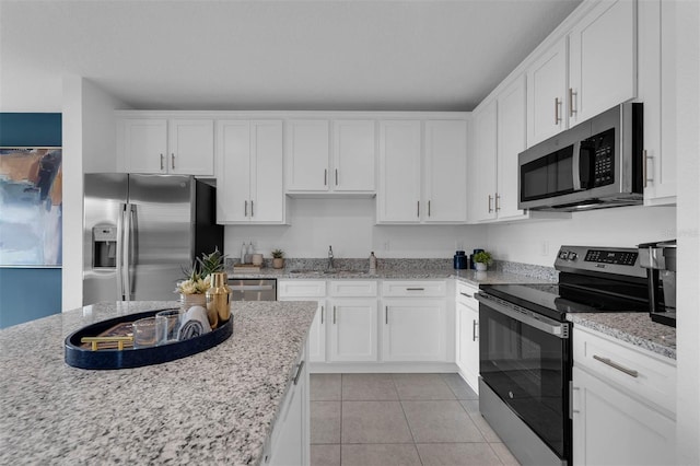 kitchen with stainless steel appliances, white cabinetry, light stone countertops, and light tile patterned flooring