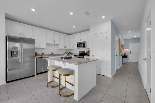 kitchen featuring appliances with stainless steel finishes, white cabinetry, a kitchen bar, a center island, and light stone counters