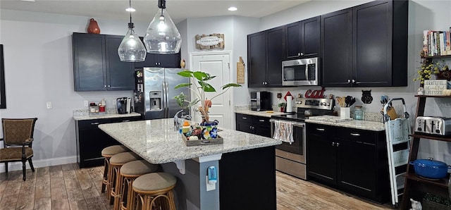 kitchen with hanging light fixtures, light hardwood / wood-style floors, stainless steel appliances, and a kitchen island with sink