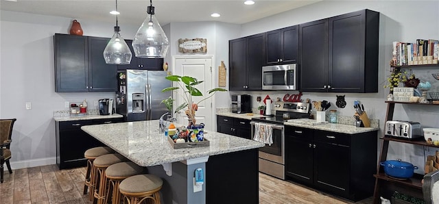 kitchen with a kitchen breakfast bar, stainless steel appliances, a center island with sink, light hardwood / wood-style flooring, and hanging light fixtures